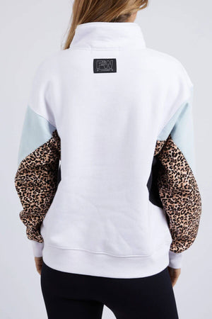 A woman is seen from behind wearing the Foxwood Splice Zip Crew, a relaxed fit white cotton sweatshirt with a black collar label, pale blue shoulder panels, and leopard print sleeves. She pairs it with black leggings.