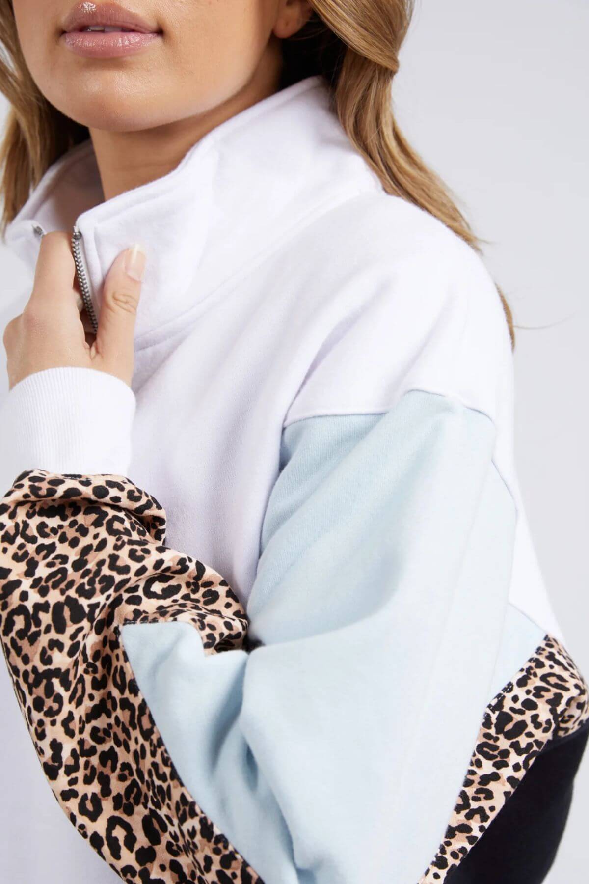 A woman models the Foxwood Splice Zip Crew, a relaxed-fit cotton jacket with light blue and leopard print color-blocked sleeves, holding the collar with only the lower part of her face visible.
