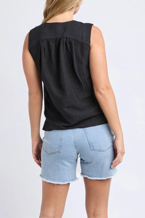 A woman is seen from the back wearing a black Foxwood Anara Top and light blue frayed denim shorts, standing against a plain light background.
