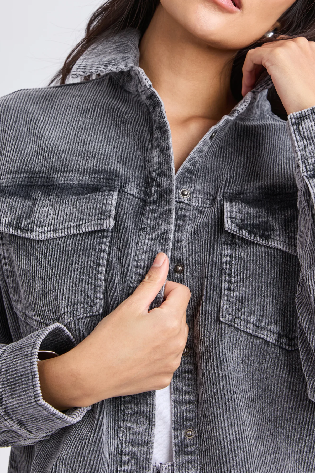 A woman adjusts the collar of the gray Foxwood Tularose Cord Shirt, highlighting its textured fabric and chest pockets. Her effortless style is showcased with her face partially out of frame.