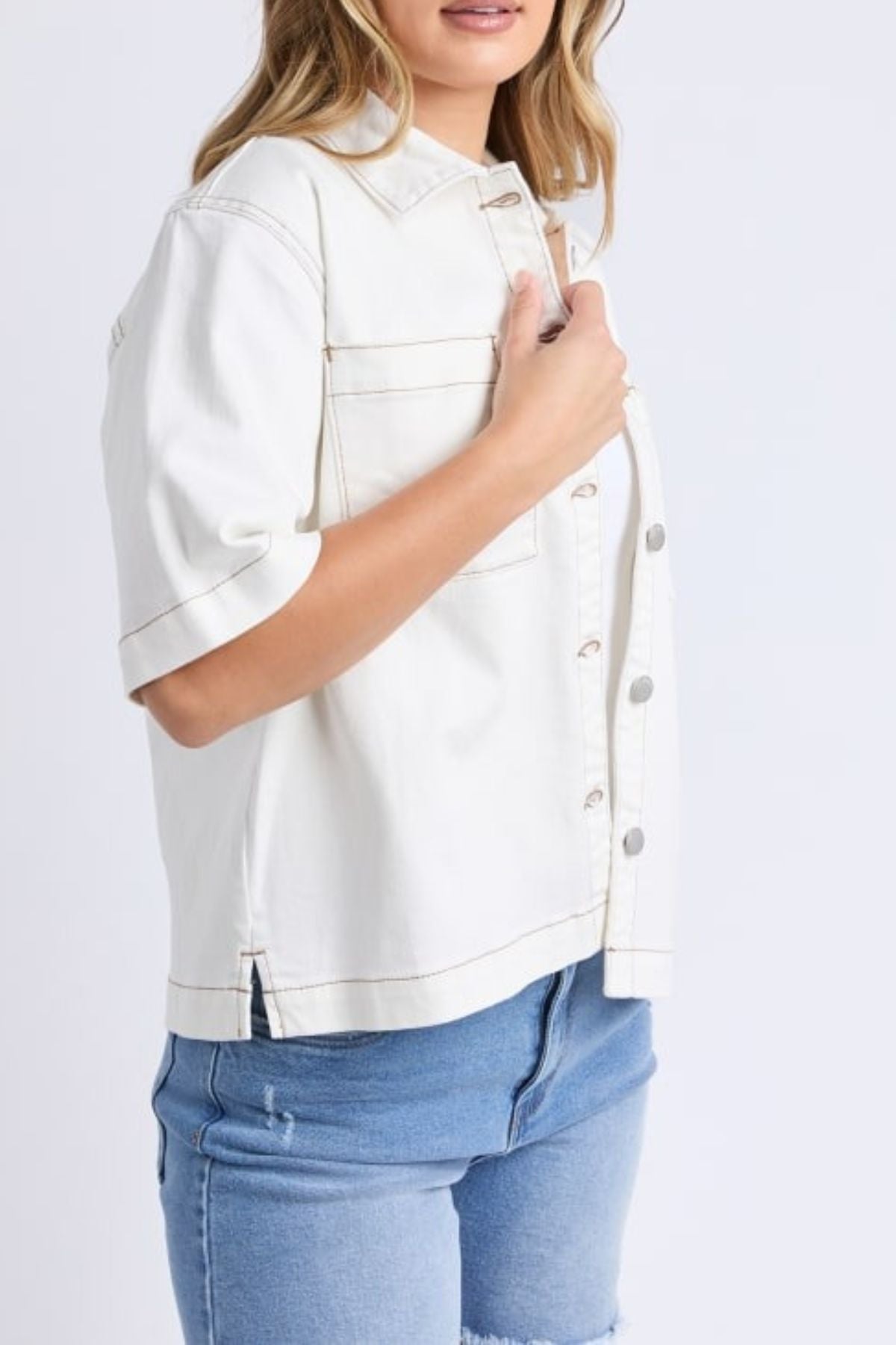 A woman models the Foxwood Valletta Short Sleeve Shirt in white, styled with blue denim shorts. She stands against a plain white background, showing only her torso and upper legs.