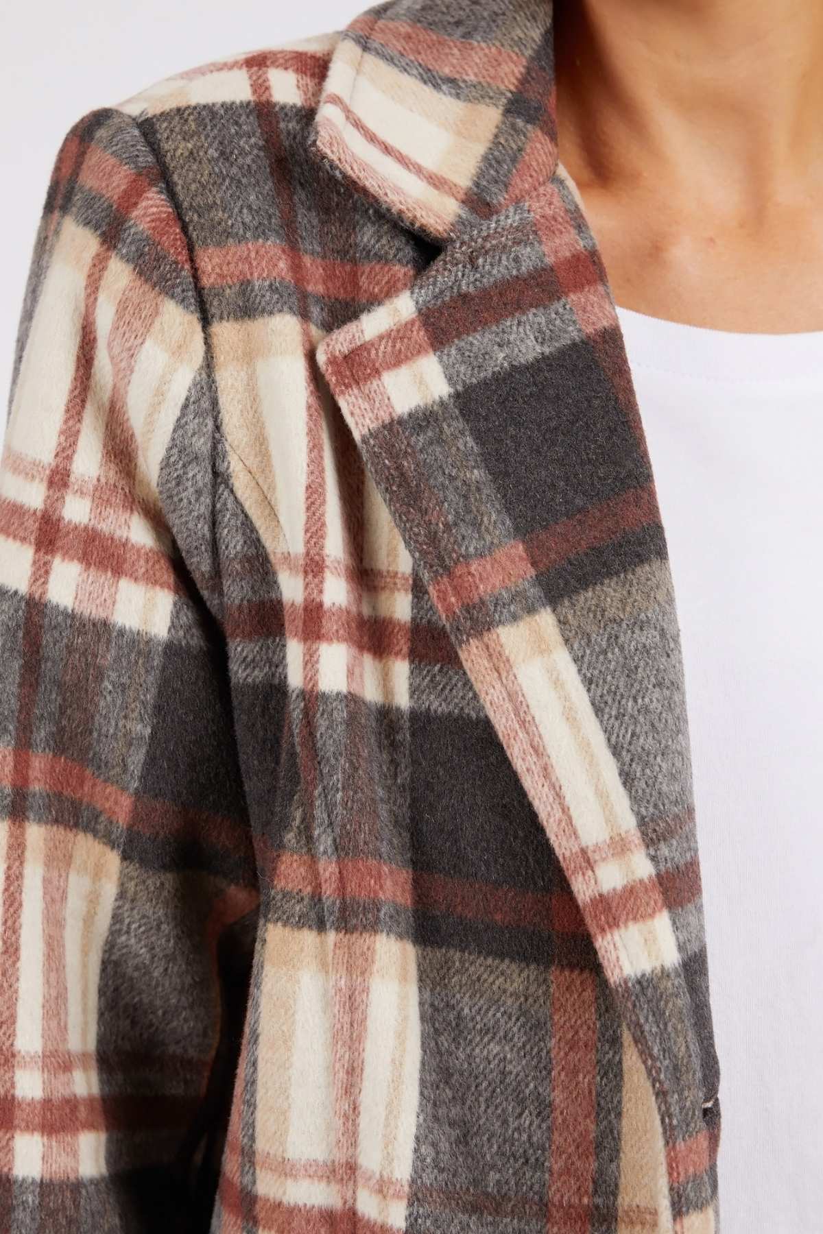 Close-up of a person in the Foxwood Westward Coat, showcasing its yarn-dyed brown, beige, and gray check pattern over a white shirt. The image focuses on the shoulder and collar of this wool-polyester blend coat.
