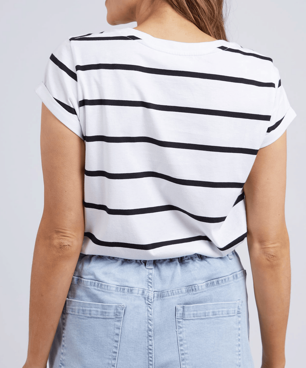 A person with long brown hair is pictured from behind, wearing a Foxwood Manly Stripe Tee and light blue denim shorts featuring rolled sleeves and an elastic waistband.