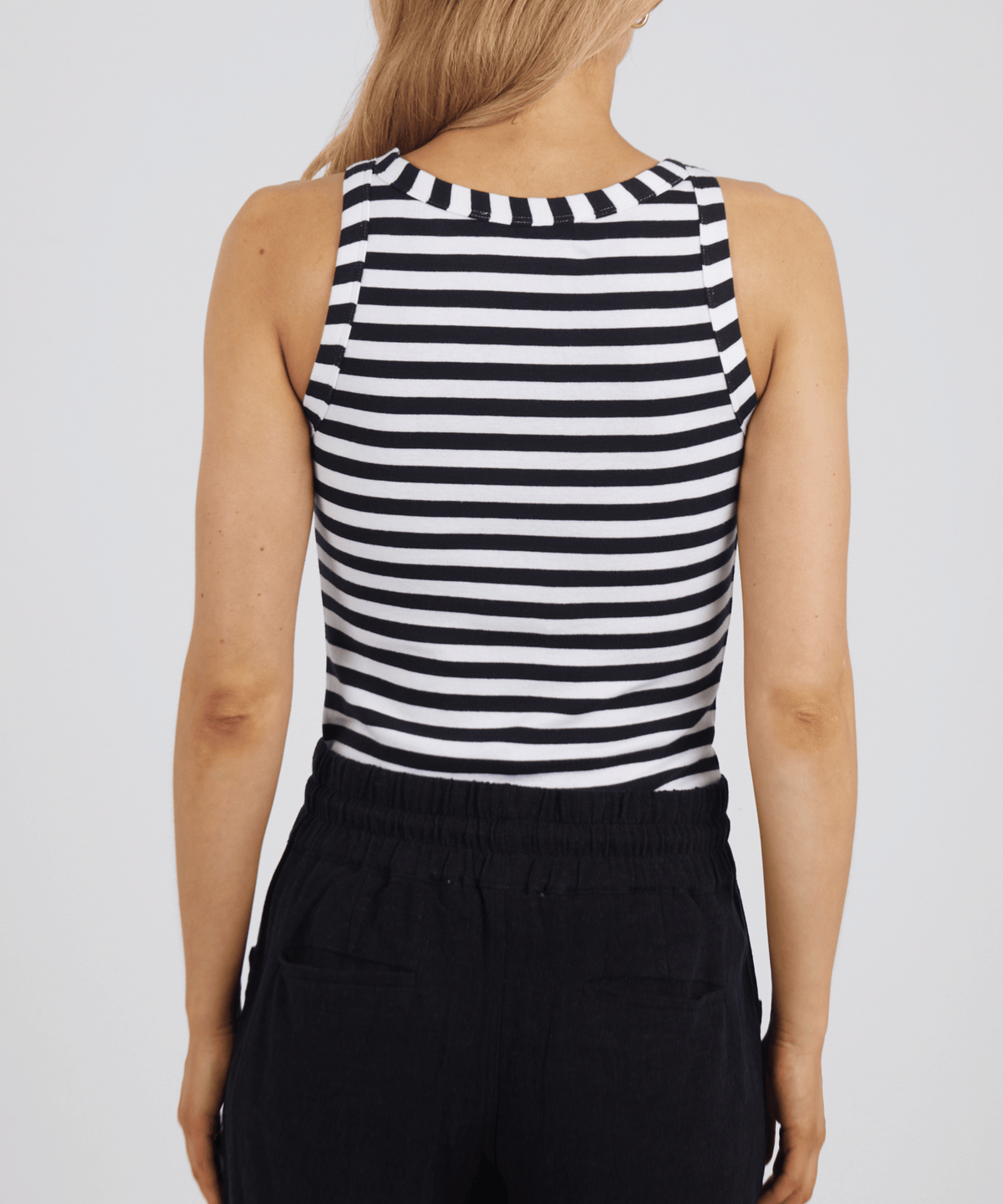 A person with long blonde hair is shown from the back, wearing the Foxwood Ruth Tank and black pants against a plain light background.