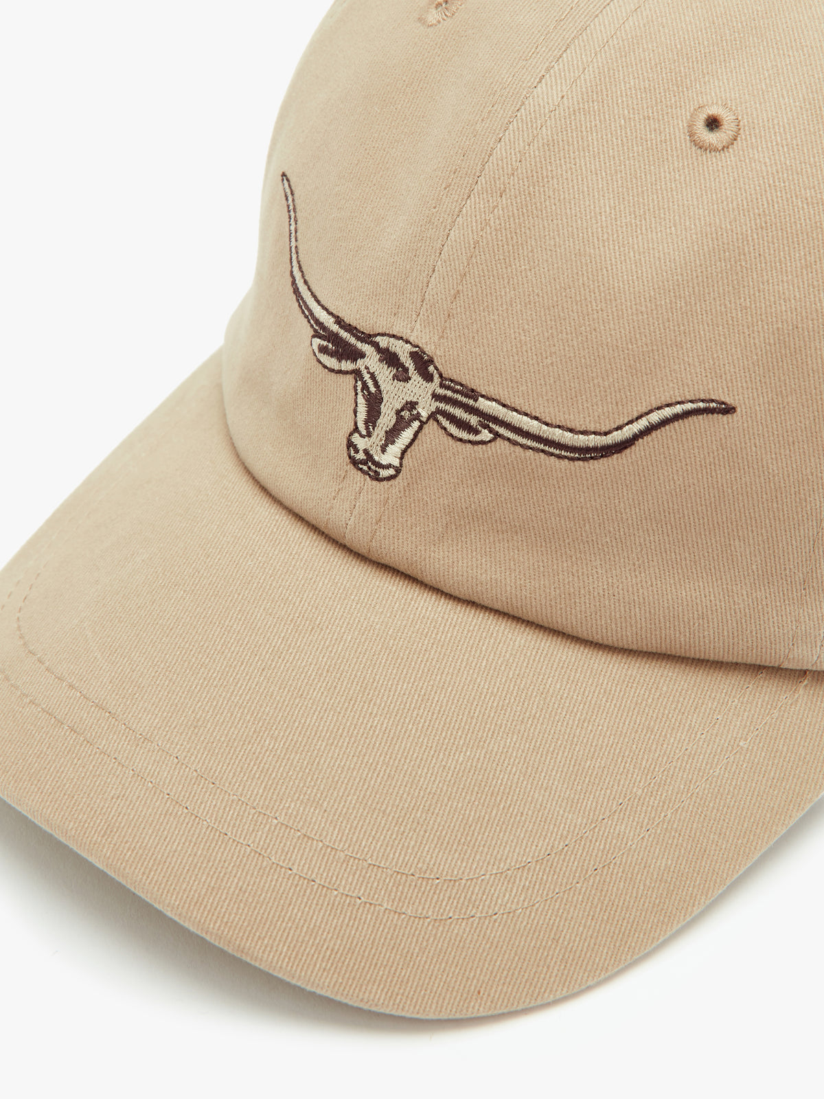 The RM Williams Longhorn Cap is a beige baseball cap made from cotton twill, featuring an embroidered longhorn steer head on the front, ventilation eyelets on the top, and an adjustable back strap.