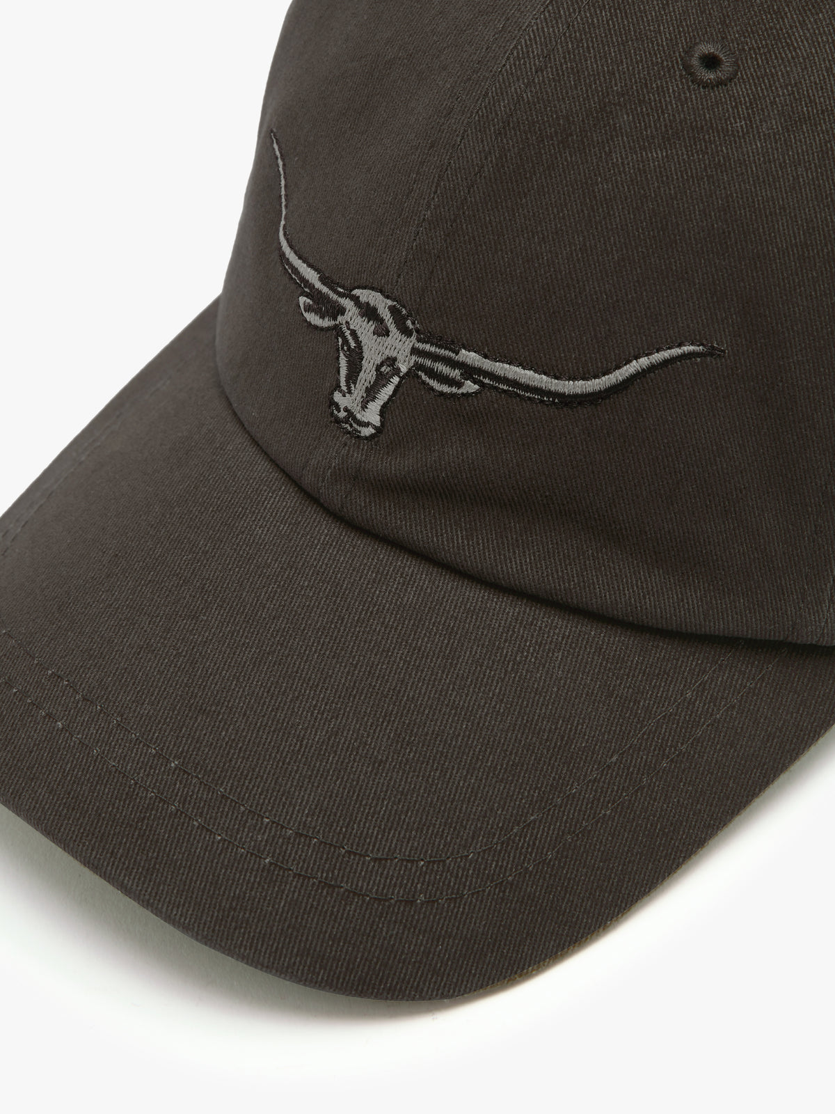 A close-up of the RM Williams Longhorn Cap in dark brown cotton twill, showcasing an embroidered longhorn skull logo on the front.