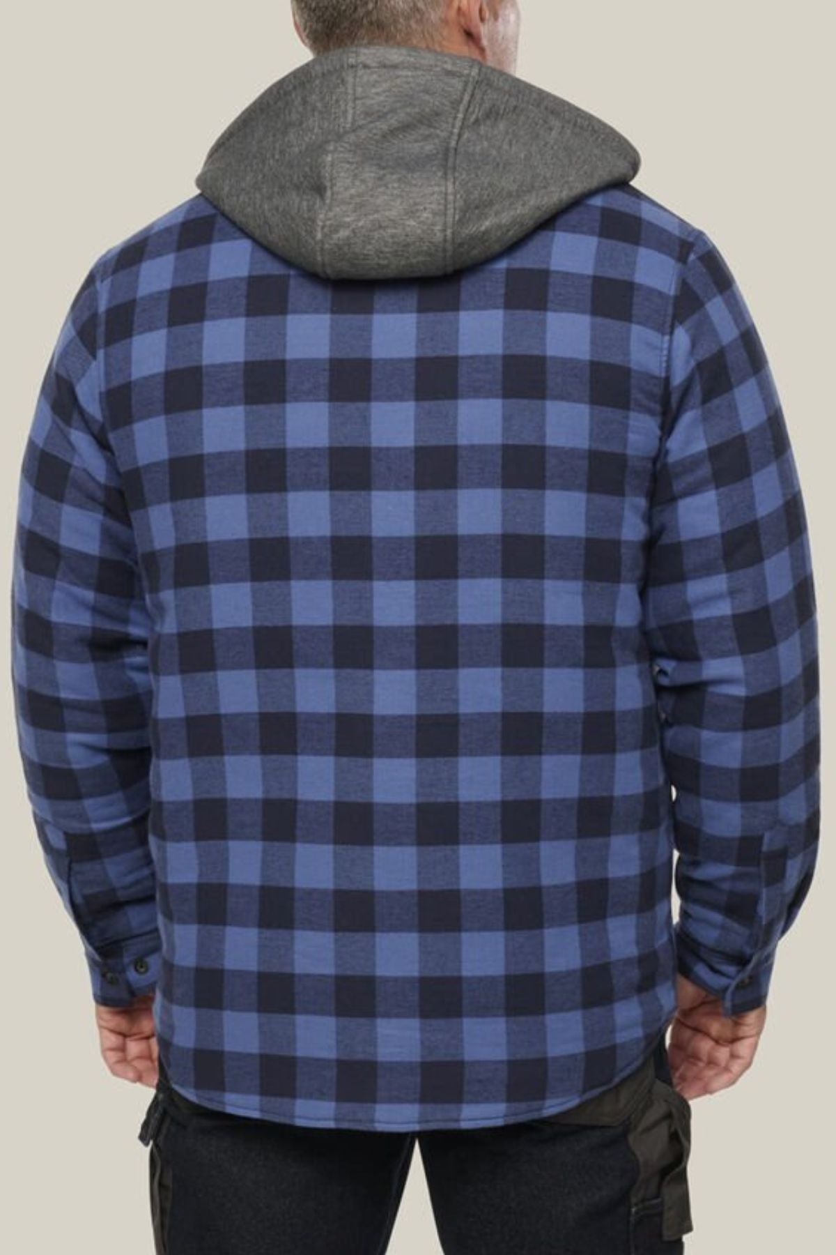 A person is seen from the back wearing a blue and black plaid Hard Yakka Quilted Flannelette Shacket with a gray hood, standing against a plain beige background.