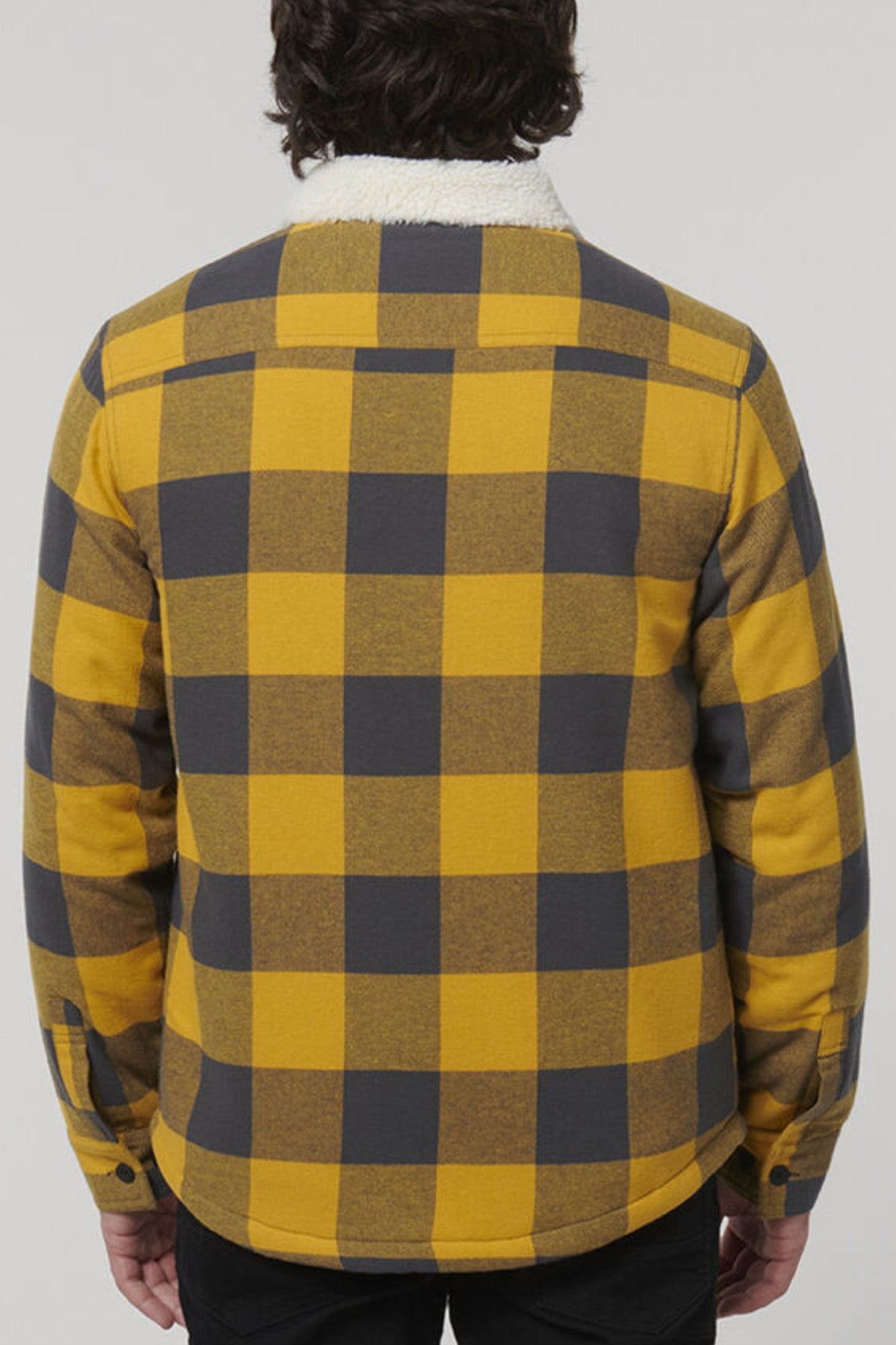 A person with dark hair is seen from behind, wearing the Hard Yakka Heritage Trucker Sherpa Jacket in yellow and black check with a white sherpa collar and black pants, against a plain light background.