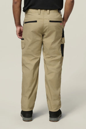 A person stands facing away from the camera, highlighting the back of the Hard Yakka Legends Slim Stretch Work Pant with utility pockets and black accents, paired with a black shirt and black shoes.
