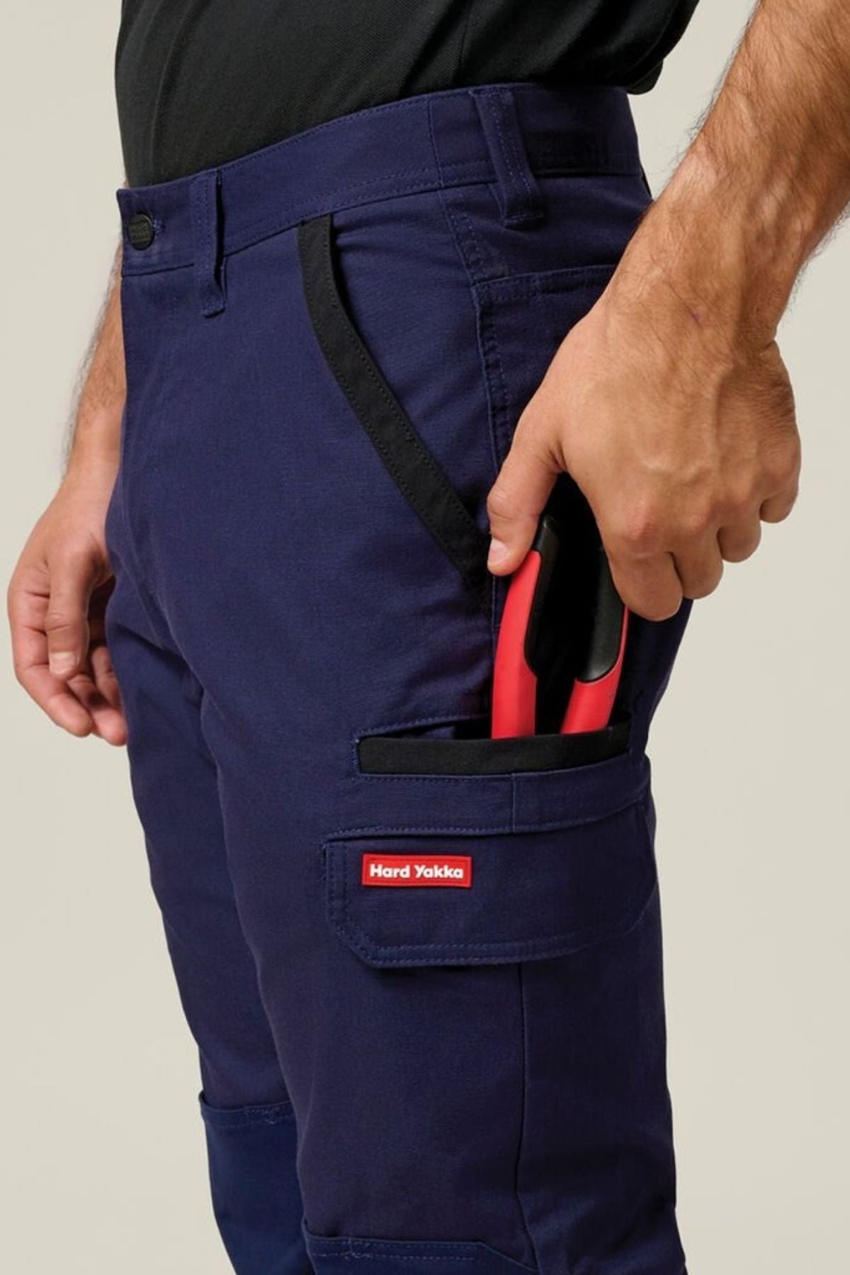 Wearing Hard Yakka Legends Slim Stretch Work Pant, a person keeps a red-handled tool partly tucked into the pant’s utility side pocket.
