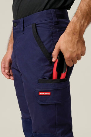 Wearing Hard Yakka Legends Slim Stretch Work Pant, a person keeps a red-handled tool partly tucked into the pant’s utility side pocket.
