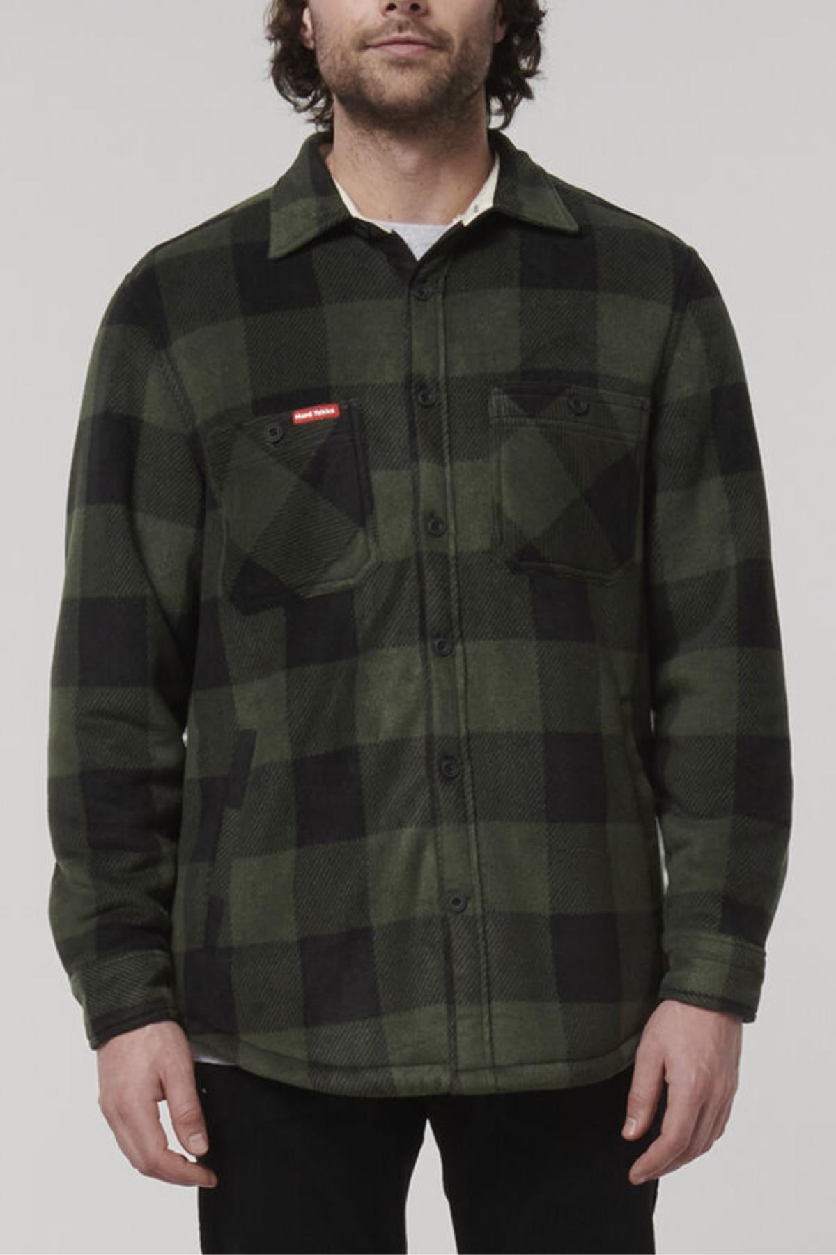 A man wearing a Hard Yakka Sherpa Bonded Fleece Jacket, featuring a green and black plaid pattern with sherpa lining. The jacket has front button closures, two chest pockets with flaps, and long sleeves. He is standing against a plain, light gray background with his face partially visible.