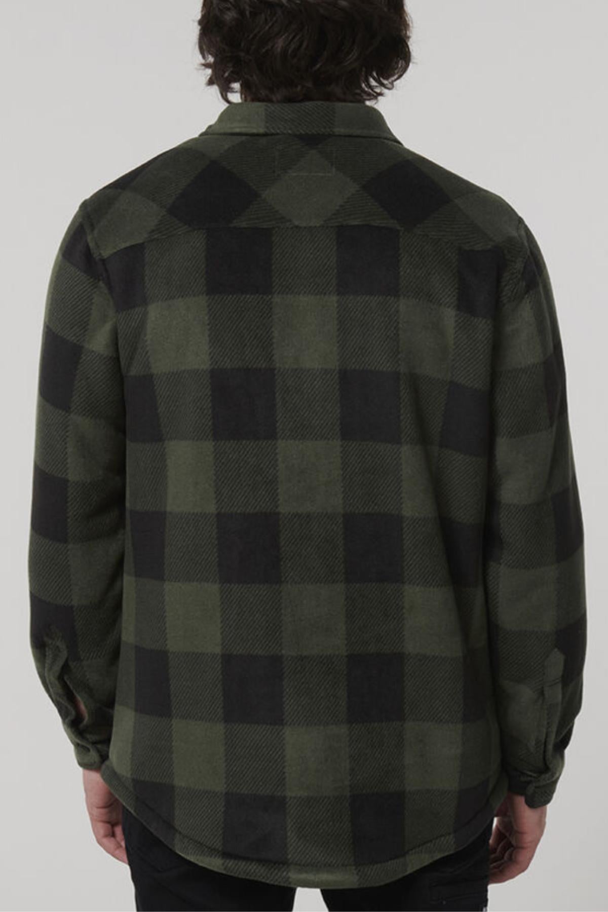 A person with medium-length dark hair is facing away from the camera, wearing a green and black checkered long-sleeve shirt that looks as cozy as a Hard Yakka Sherpa Bonded Fleece Jacket. The background is plain and light-colored.