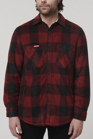 A person wearing a red and black checkered flannel shirt with adjustable cuffs and two chest pockets, one of which has a label, that resembles the rugged style of the Hard Yakka Sherpa Bonded Fleece Jacket. The person has light skin and dark hair, and their face is not fully visible against the plain light gray background.