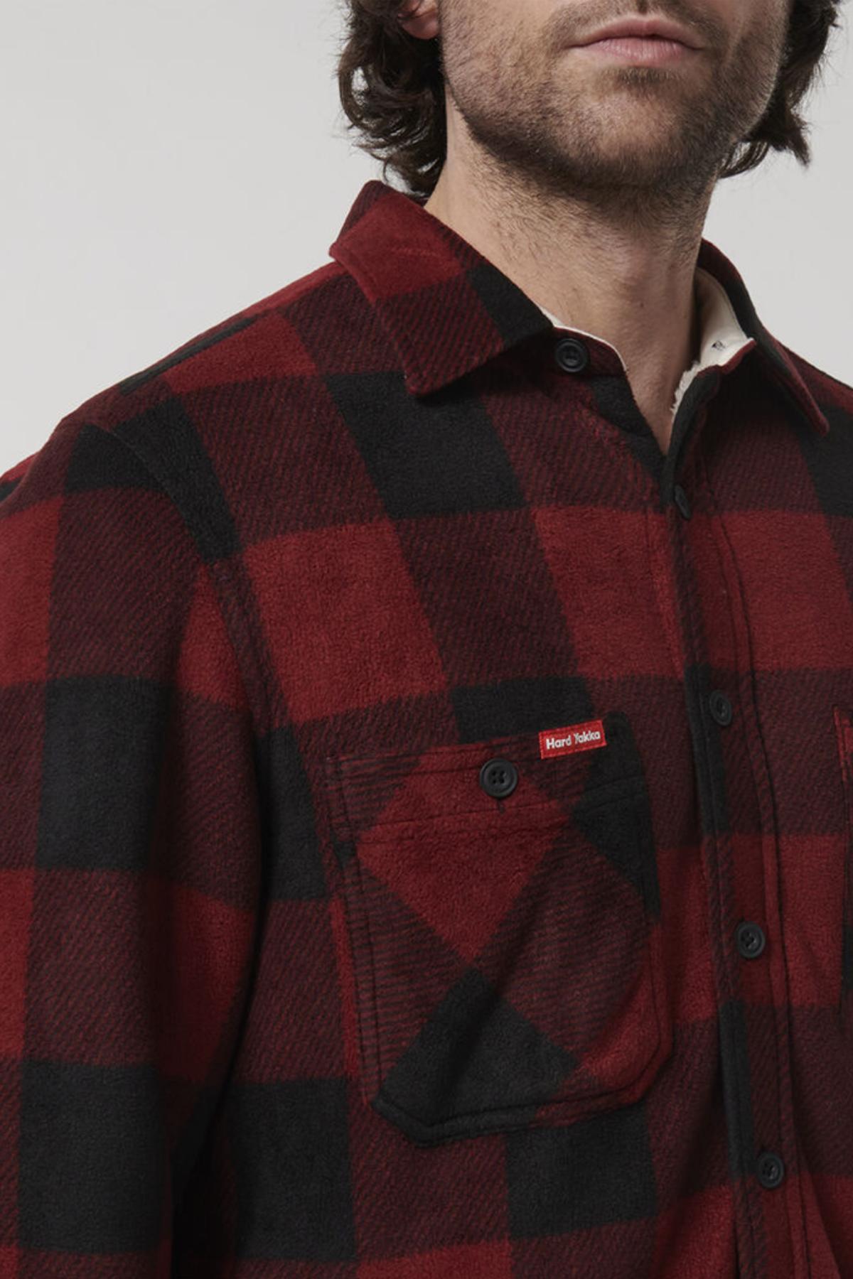A man is partially visible wearing a Hard Yakka Sherpa Bonded Fleece Jacket. The jacket features adjustable cuffs and a front chest pocket with a small red tag. The man's face is mostly out of frame, and the background is plain and light-colored.