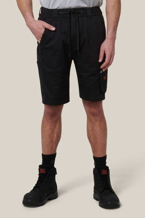 A person wearing a white t-shirt, Hard Yakka Tough Maxx Mid Short with an elastic waistband and drawstring, black socks, and black lace-up boots stands against a plain light beige background.