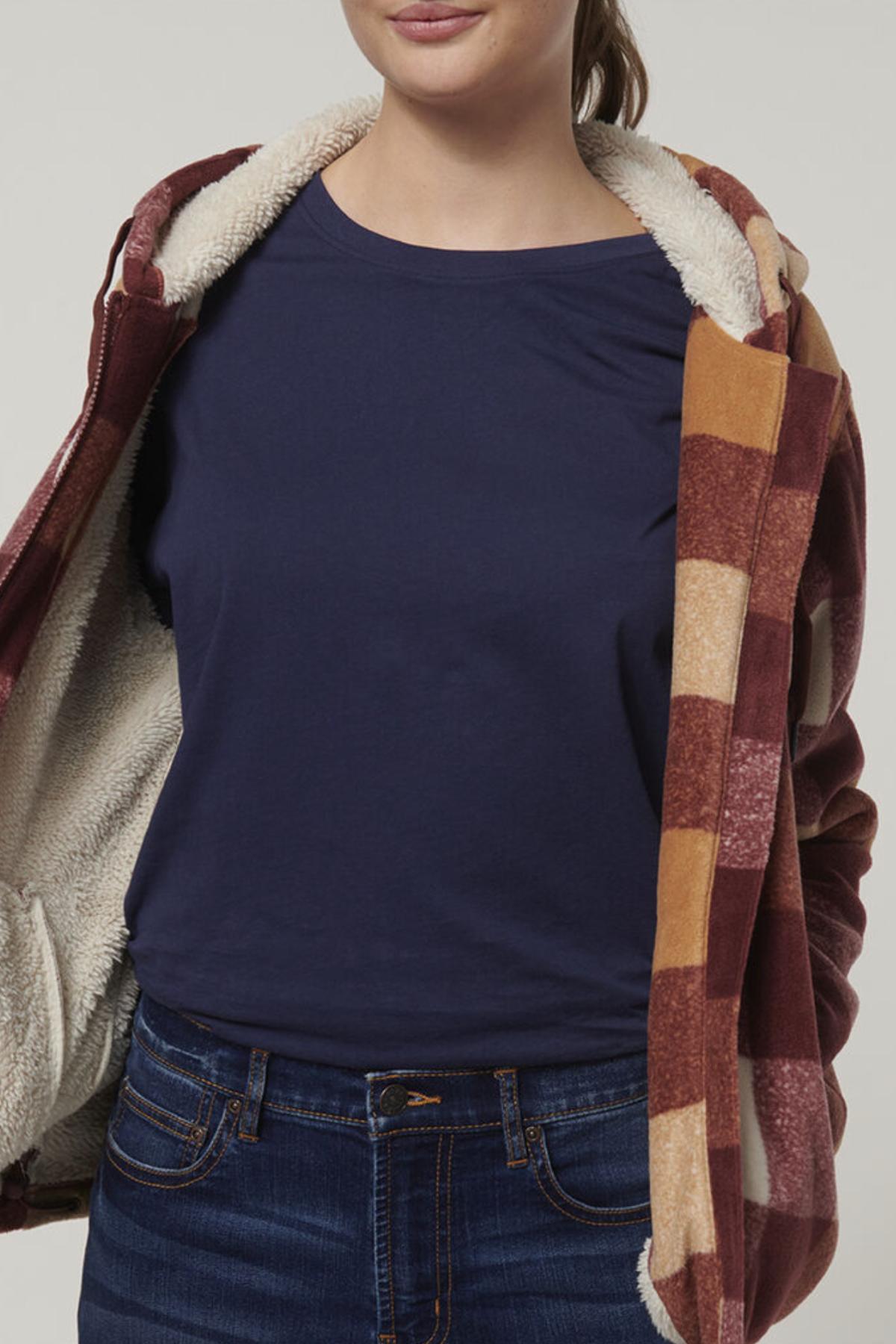 A person wears the Hard Yakka Womens Check Zoodie, featuring maroon, tan, and cream checks with a cozy sherpa lining over a navy blue t-shirt and jeans. The zoodie is open, showing its fleece body; the person's face is partly out of frame.