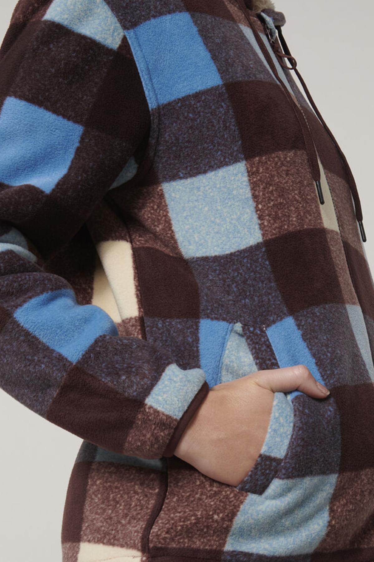 A close-up shows a person in the Hard Yakka Womens Check Zoodie, featuring a blue, brown, and cream check fleece with drawstrings and front pocket. The hoodie provides thermal insulation for warmth.