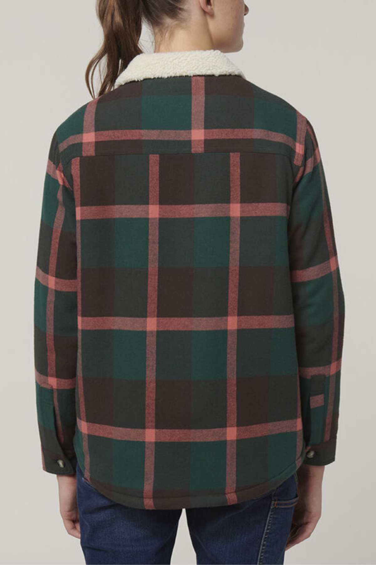 A woman with brown hair in a ponytail wears the Hard Yakka Women's Heritage Trucker Sherpa Jacket, featuring green, red, and black plaid with a white sherpa collar, shown from the back against a plain background.