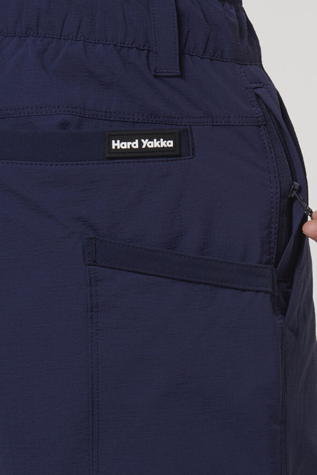 Close-up of a hand pulling a zipper next to the pocket of Hard Yakka X Short Short, showing durable Cordura Nylon fabric and the visible "Hard Yakka" label above the pocket.