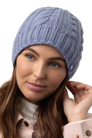 A woman with long brown hair is wearing a Heat Holders Alesund Ladies Thermal Beanie in light purple. She is seen touching the edge of the beanie with one hand. Dressed in a light-colored jacket, she looks slightly off to the side with a gentle expression against a white background.