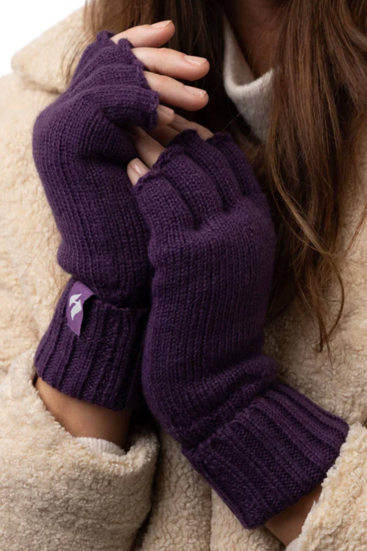 A person in a beige fuzzy coat and white turtleneck displays purple Heat Holders Ladies Fingerless Thermal Gloves, featuring HeatWeaver lining for outstanding insulation and comfort.