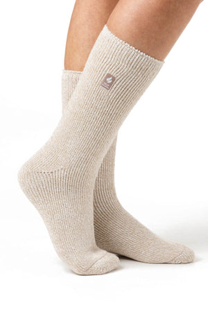 Close-up of a person wearing Heat Holders Ladies Original Thermal Heat Socks in light beige, featuring a ribbed design and crew-length fit. These warm and cozy socks include a small brown tag with a logo near the top and boast an impressive TOG rating of 2.3. The background is plain white, focusing solely on the knees-down view.