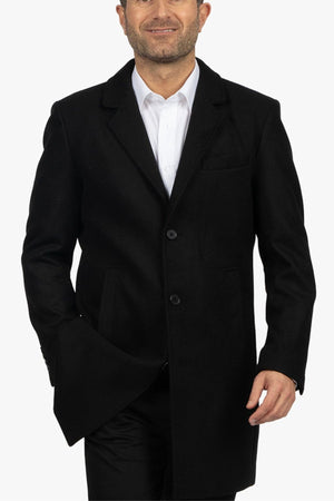 A man wearing the Howard Hudson Overcoat over a white dress shirt smiles as he walks forward against a plain white background.