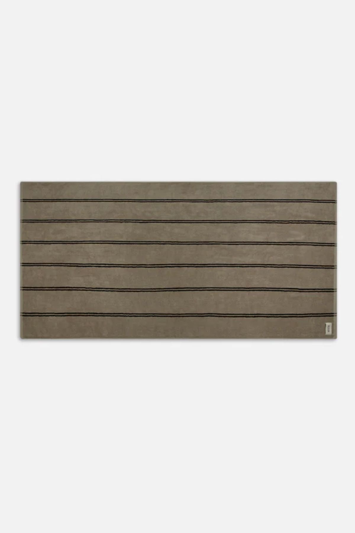 The Industrie Comporta Beach Towel is rectangular, brown, and features thin black horizontal lines inspired by halo stripes with a small logo in the bottom right corner.