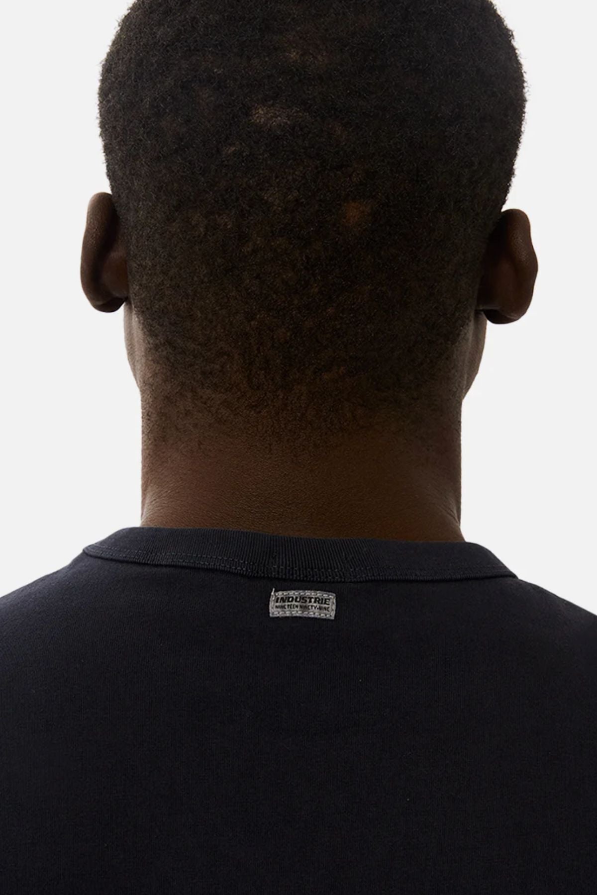 A close-up of the back of a person’s head and neck, showing short dark hair. They are wearing the Industrie The Del Sur Sleeveless Tee, featuring a small rectangular label on the back collar.