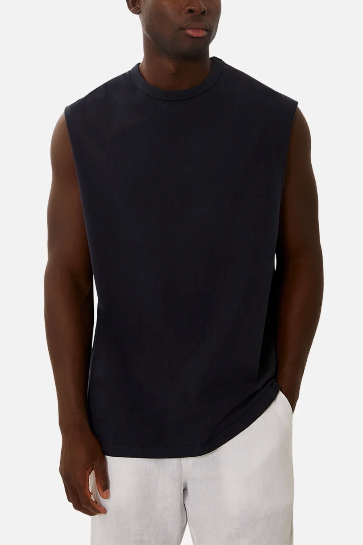 A man wearing the Industrie The Del Sur Sleeveless Tee in black with light shorts stands with one hand in his pocket against a plain light background.
