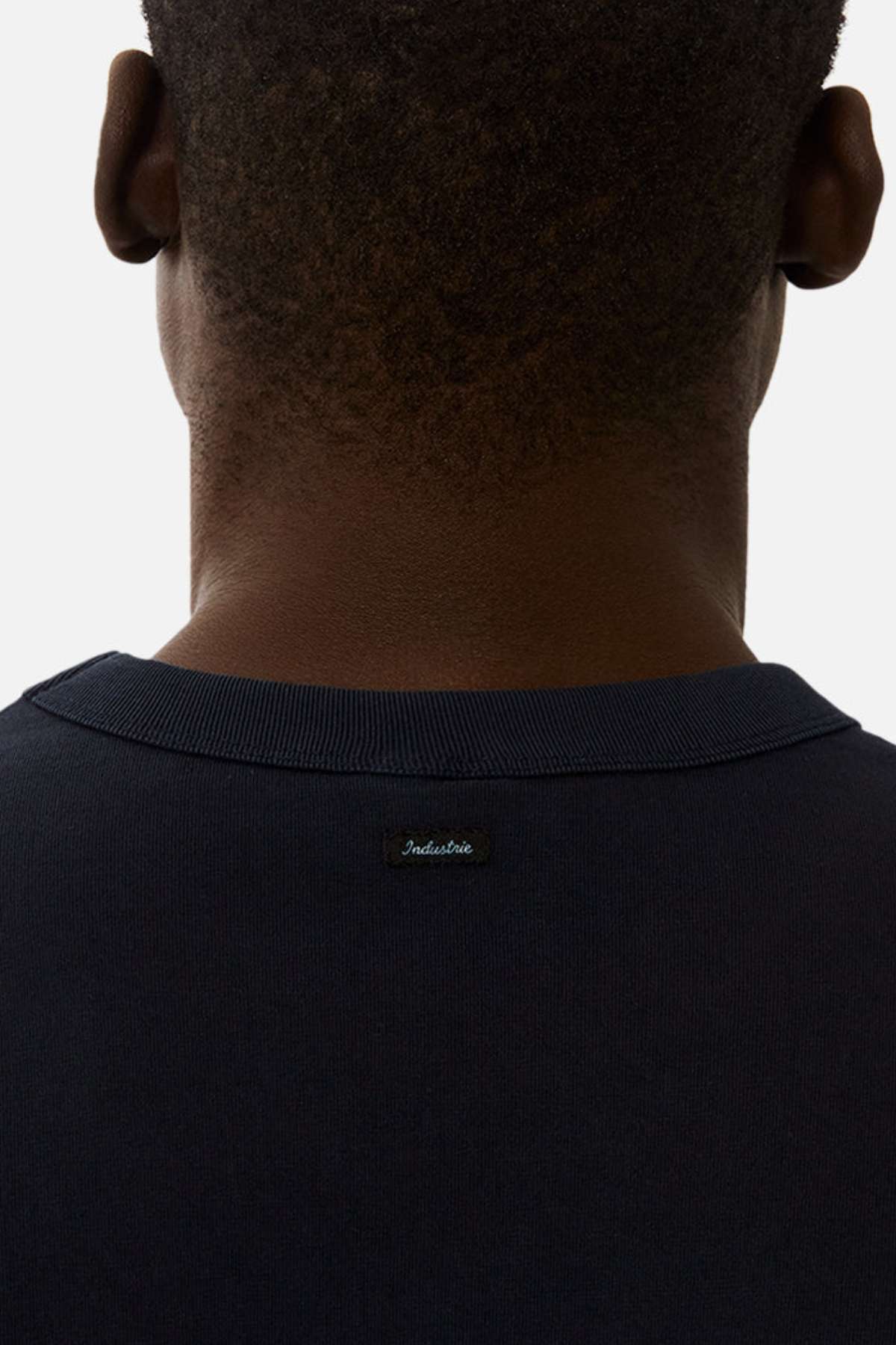 A close-up of the back of a person wearing the Industrie The Del Sur Tee, an oversized dark tee made from 100% cotton, featuring a small "Industrie" label on the upper back.