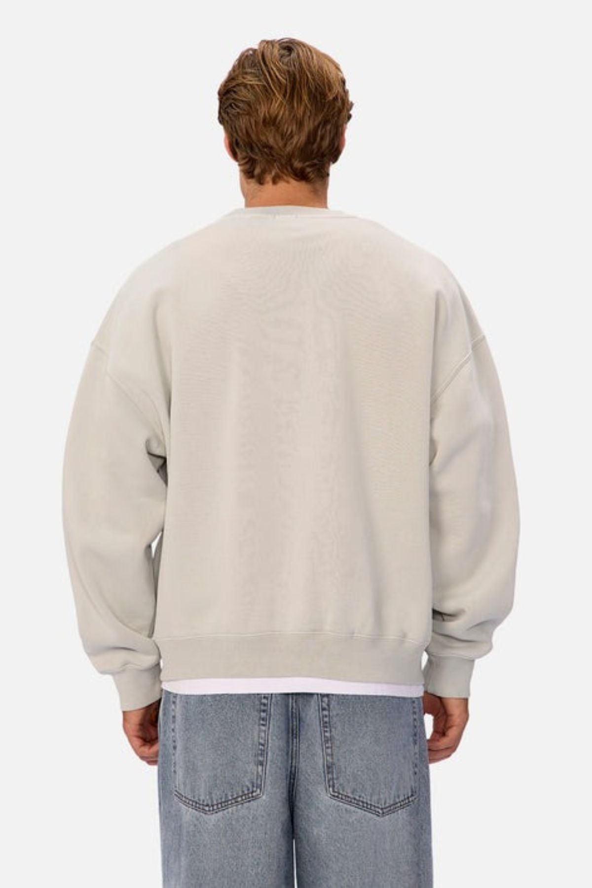 A person with short, light brown hair is shown from behind wearing an oversized Industrie The New Del Sur Washed Sweat over a white shirt and loose blue jeans against a plain white background.