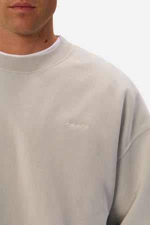 A person wears the Industrie The New Del Sur Washed Sweat in light grey, oversized fit, with "Industrie" embroidered on the left chest. Only the lower half of their face and upper torso are shown against a plain white background.