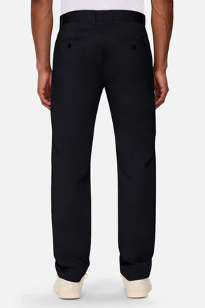 A person stands facing away from the camera in Industrie The Regular Cuba Chino Pant, a stretch cotton blend with a wide leg fit, belt loops, and two buttoned back pockets, paired with a white shirt and white sneakers.