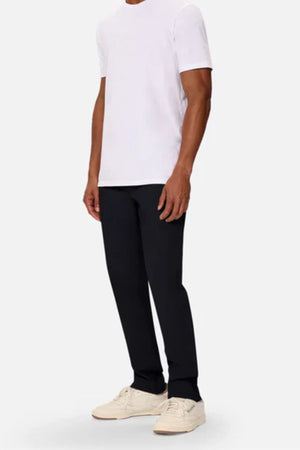 A person wearing a plain white T-shirt, Industrie The Regular Cuba Chino Pant in a wider leg fit, and off-white sneakers stands against a light gray background with their head not visible.