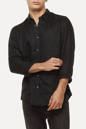 A person in an Industrie The Tennyson Linen Shirt with rolled-up sleeves and relaxed-fit black pants stands against a plain white background.