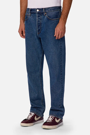 Someone wearing Industrie The 90's Jean in classic blue, a white t-shirt, and maroon and white Nike sneakers stands against a plain light background. The image is cropped from shoulders to feet.