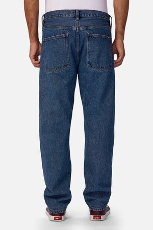 A person is seen from behind wearing Industrie The 90's Jean—relaxed, straight-leg, 100% cotton vintage-washed denim with two large back pockets and visible stitching—paired with red Nike sneakers against a plain white background.