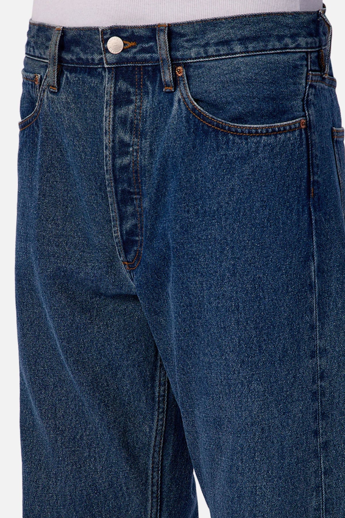 Close-up of a person wearing Industrie The 90's Jean, made from 100% cotton vintage washed denim with front pockets, metal button, and zipper fly, paired with a tucked-in white shirt.