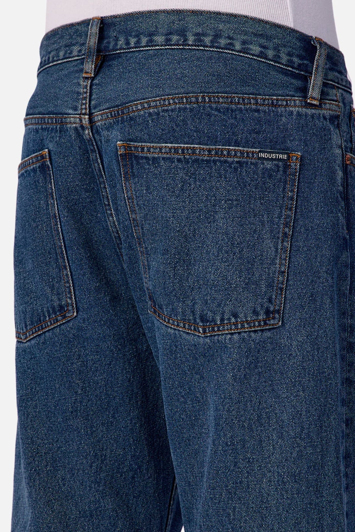 Close-up of the back of a person wearing Industrie The 90's Jean, vintage washed denim with relaxed straight legs, two rear pockets, and a small "Industrie" label above the right pocket.