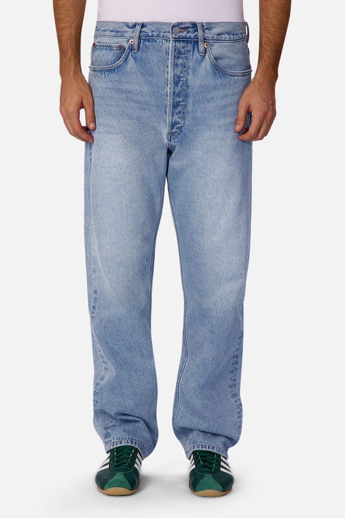 A person wearing Industrie The 90's Jean in vintage washed denim and green sneakers stands with hands relaxed by their sides against a plain background, showing only the legs and lower torso.
