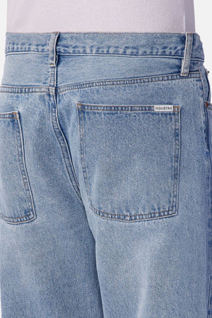 Close-up of the back of a person wearing Industrie The 90's Jean—vintage washed, light blue relaxed straight leg jeans with two back pockets, a small white INDUSTRIE label above the right pocket, and a light shirt visible at the waist.