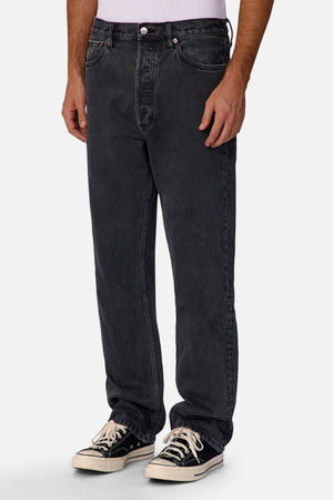 A person models Industrie The 90's Jean in vintage washed denim, paired with a white shirt and black-and-white lace-up sneakers against a plain white background, showing only their lower torso and legs.