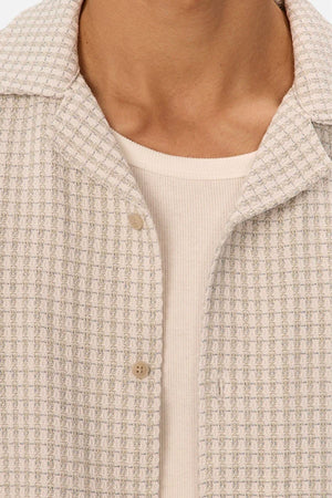 Close-up of a person wearing the Industrie The Almeria Short Sleeve Shirt in a light shade, layered over a cream ribbed top. Only the neck, upper chest, and shirts are visible.
