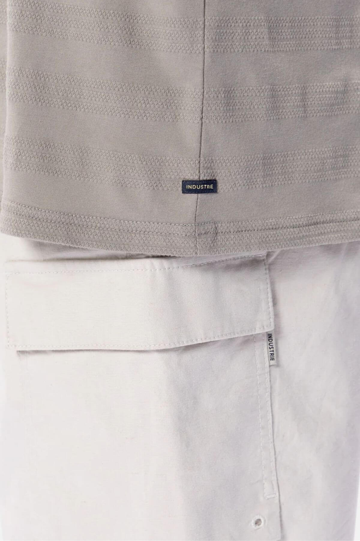 Close-up of a person wearing the Industrie The Anderson Textured Stripe Tee in light grey, paired with white pants featuring a large pocket and an Industrie label near the seam.