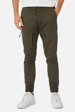 A person wears Industrie The Armoured Drifter Pant in olive green with zippered cargo pockets and white drawstrings, paired with white sneakers—shown from the waist down against a plain background, ideal for any adventurer.