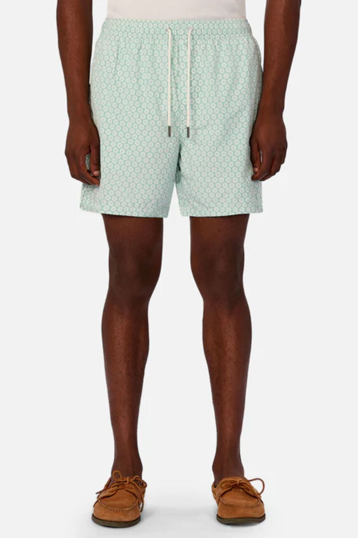 A person wears Industrie The Aruba Swim Short in light blue print with a white drawstring, paired with a white shirt and brown moccasins, standing against a plain background.