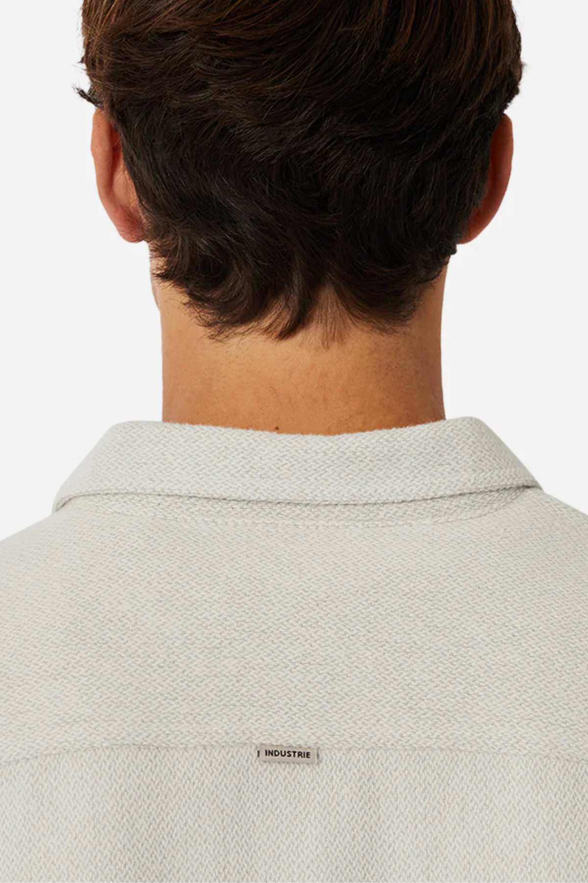The image shows the back of a person with short brown hair wearing the Industrie The Atacama Shirt, featuring a light textured fabric, collared design, and an "INDUSTRIE" tag on the upper back for a classic look.