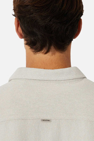 The image shows the back of a person with short brown hair wearing the Industrie The Atacama Shirt, featuring a light textured fabric, collared design, and an "INDUSTRIE" tag on the upper back for a classic look.